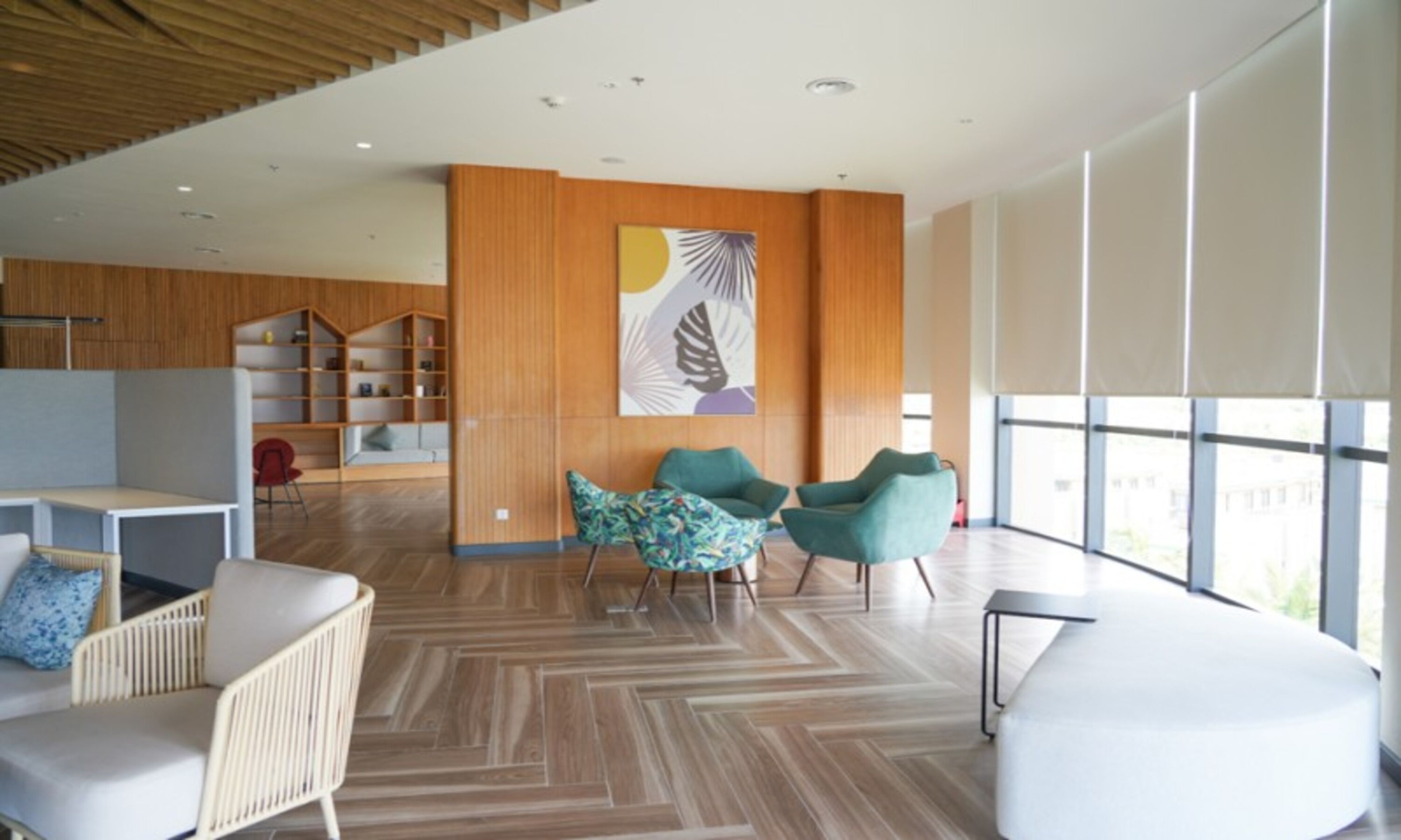 A modern interior with a herringbone wood floor, a large window with a view, and a seating area with a white sofa and two teal chairs.