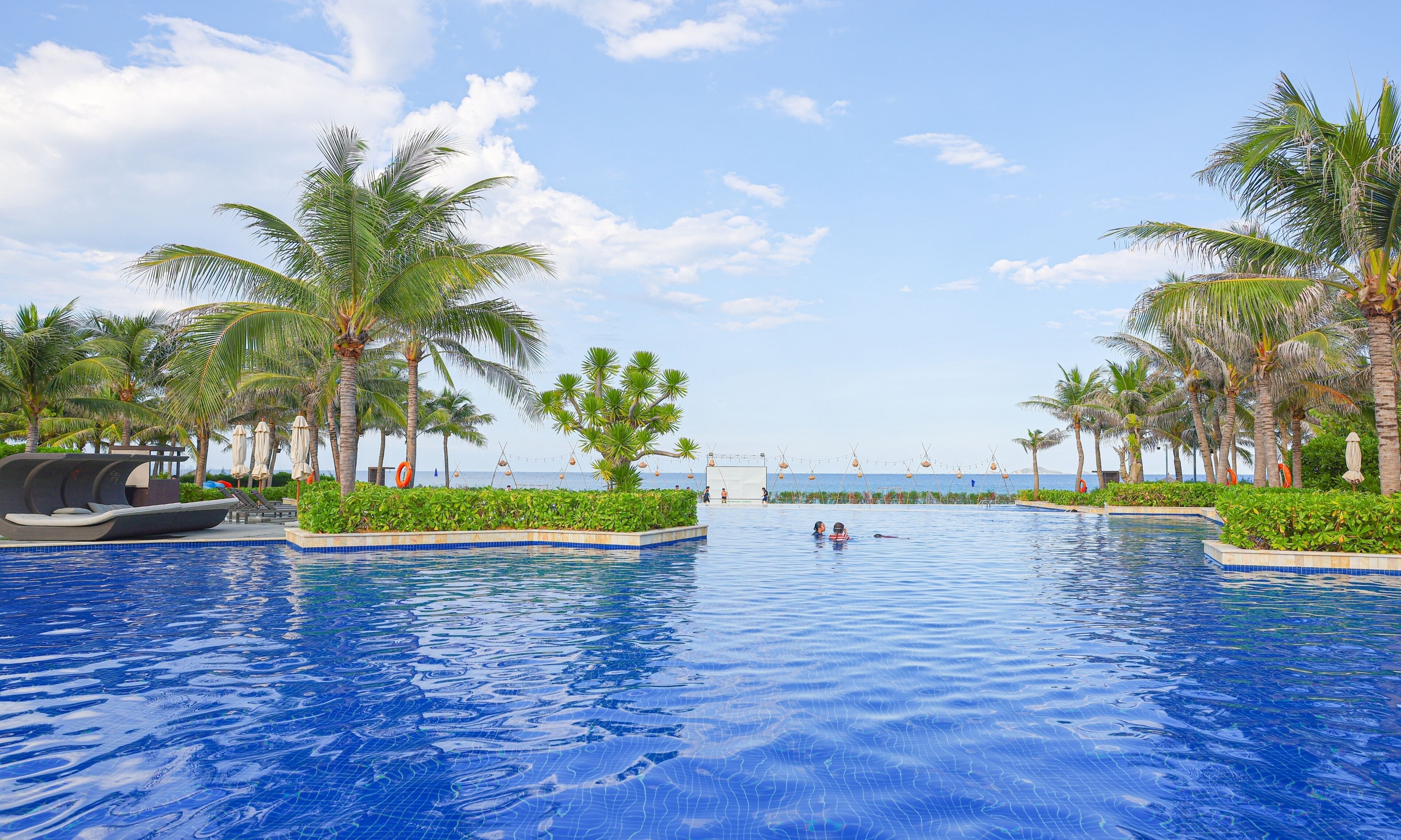 A large outdoor swimming pool surrounded by palm trees and a clear sky.