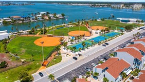 Un complejo deportivo costero con campos de béisbol, piscina y una carretera con coches estacionados.