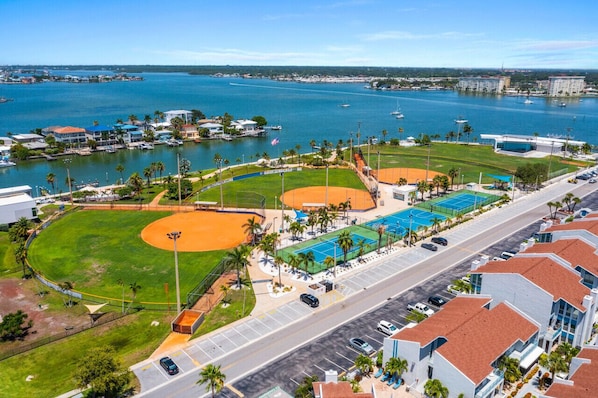 A coastal sports complex with baseball fields, a swimming pool, and a road with parked cars.