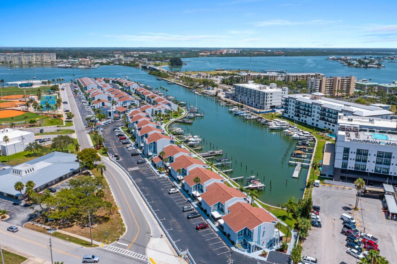 A marina with boats docked, a road lined with buildings, and a clear view of the water.