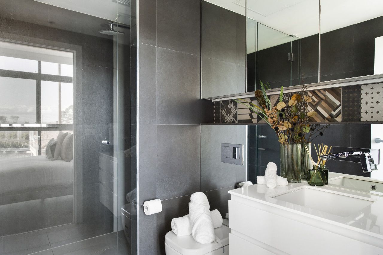 A modern bathroom with a glass shower enclosure, a white sink, and a large mirror.
