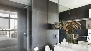 Un baño moderno con cabina de ducha de vidrio, lavamanos blanco y un espejo grande.