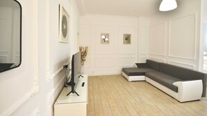 Een moderne woonkamer met een hoekbank, een flatscreen televisie en een hanglamp.