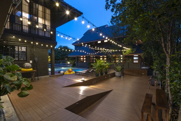 A wooden deck with string lights, a pool, and potted plants.
