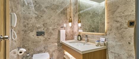 A modern bathroom with a marble wall, a wooden vanity, a white sink, and a large mirror.