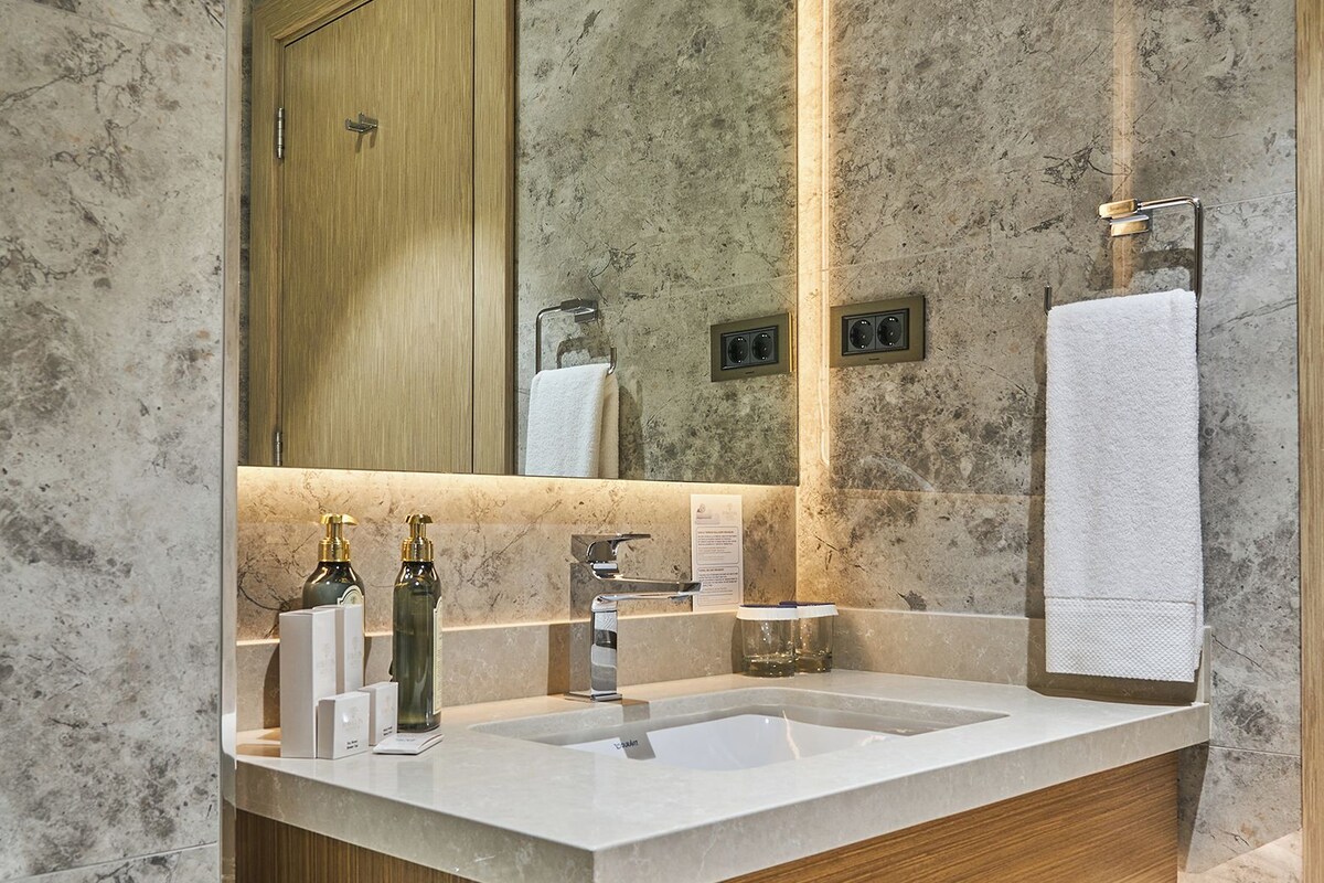 Un baño con pared de mármol, tocador de madera y un espejo grande.