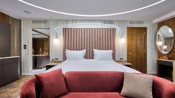 A modern hotel room with a large bed, a red sofa, a wooden door, and a mirror.