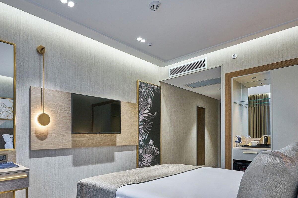 Una habitación de hotel moderna con una cama grande, un televisor montado, un espejo amplio y un equipo de aire acondicionado de pared.