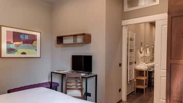 Et hotelværelse med en seng, et skrivebord med en computer, en stol, et billede i ramme på væggen og et badeværelse, der kan ses gennem en åben dør.