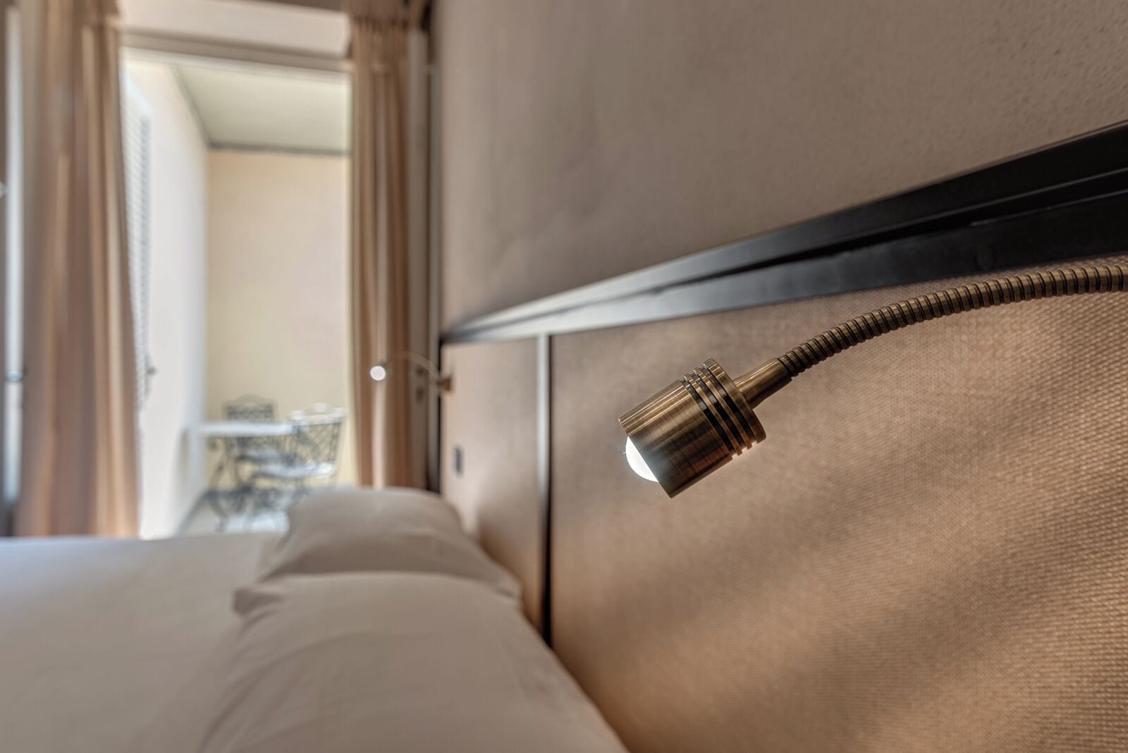 A bed with a headboard, a bedside lamp, and a view of a room with a door and a table.