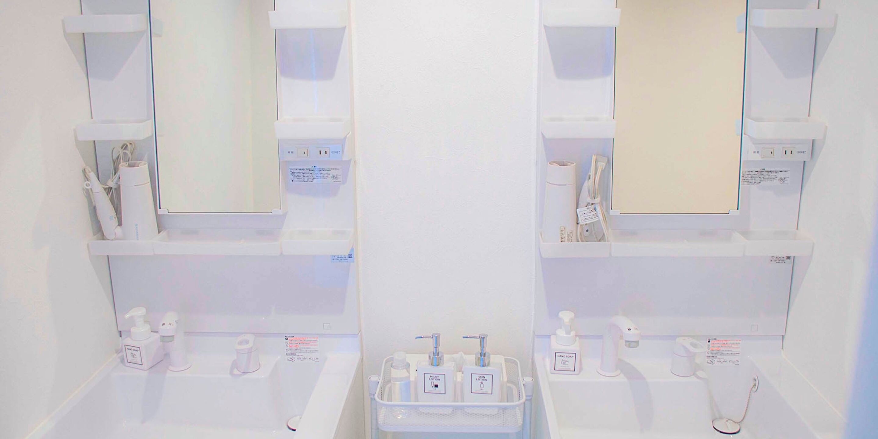 A bathroom with two sinks, each with a mirror above. There are toiletries on the sinks and shelves above.