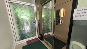 Entrada de un hotel con puertas de vidrio, un felpudo verde y un cartel que indica tarifas de alquiler de playa.
