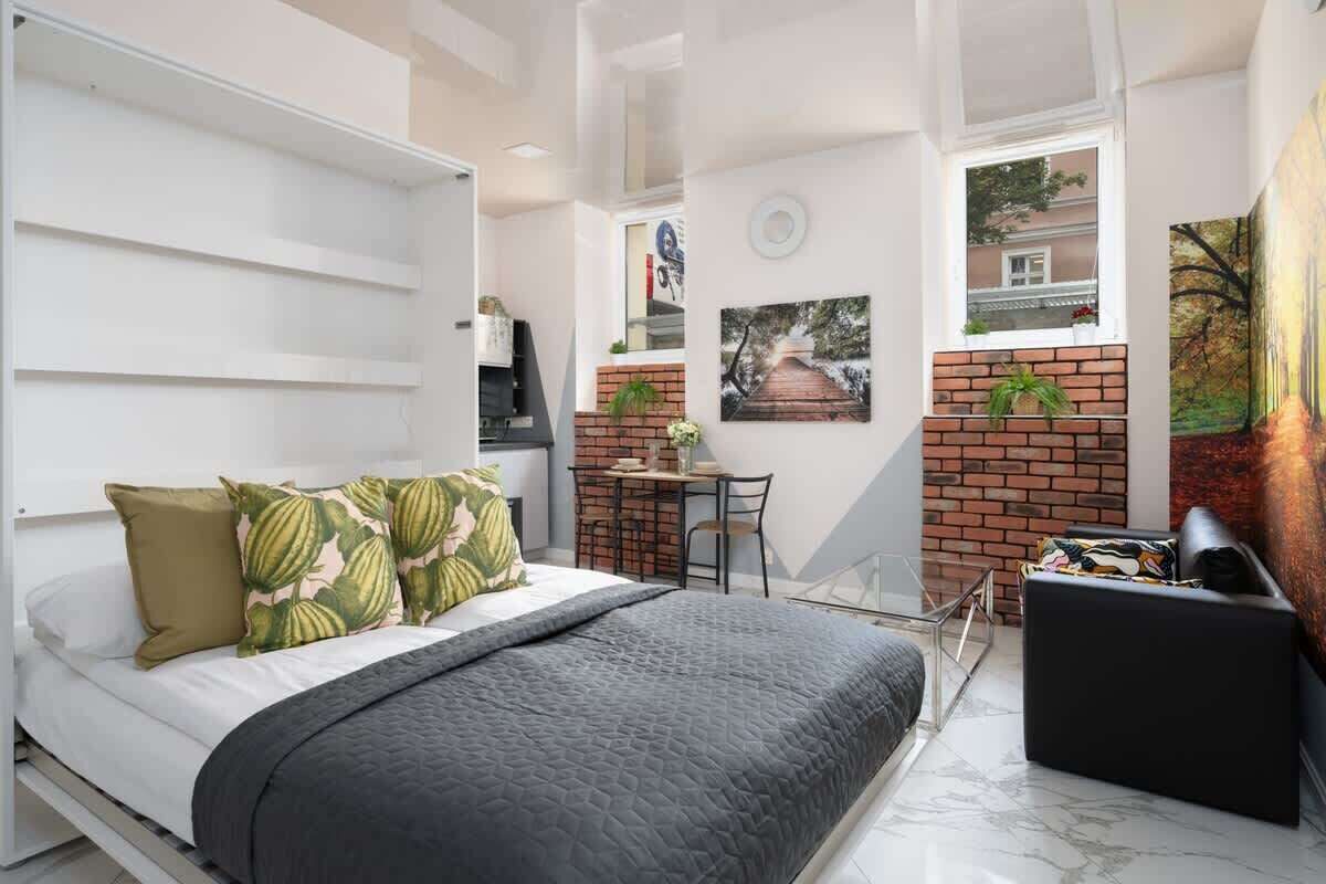 Stylish studio apartment featuring a cozy bed with decorative pillows, modern furnishings, and brick accents.

