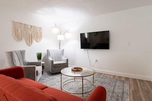Un salon moderne avec un téléviseur à écran plat, deux fauteuils, une table basse ronde et un canapé rouge.
