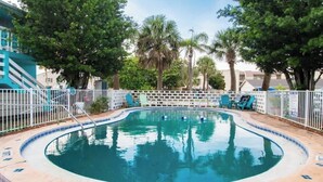 Una piscina con borde curvo, rodeada por una valla blanca y árboles al fondo.