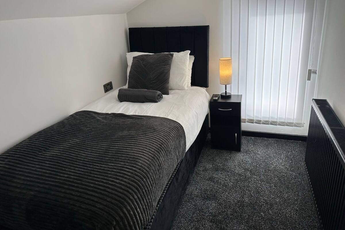 A hotel room with a bed, a nightstand, a lamp, and a window with blinds.