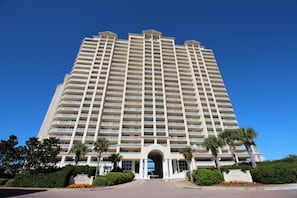 A tall, multi-story hotel with a central entrance, surrounded by palm trees and well-maintained landscaping.