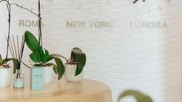 A reception desk with potted plants and a wall clock displaying 'ROME', 'NEW YORK', and 'LONDA'.
