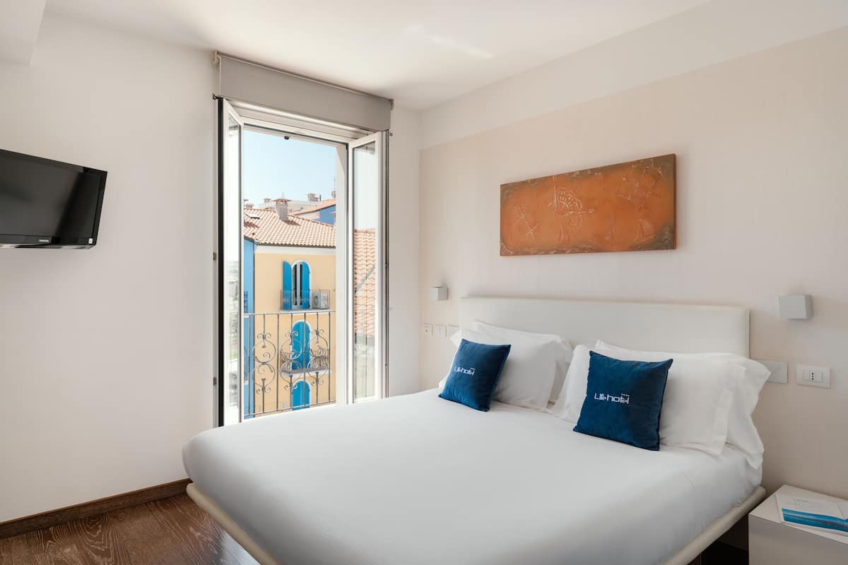 Una habitación de hotel con una cama, un televisor montado en la pared y un ventanal con vistas a edificios.