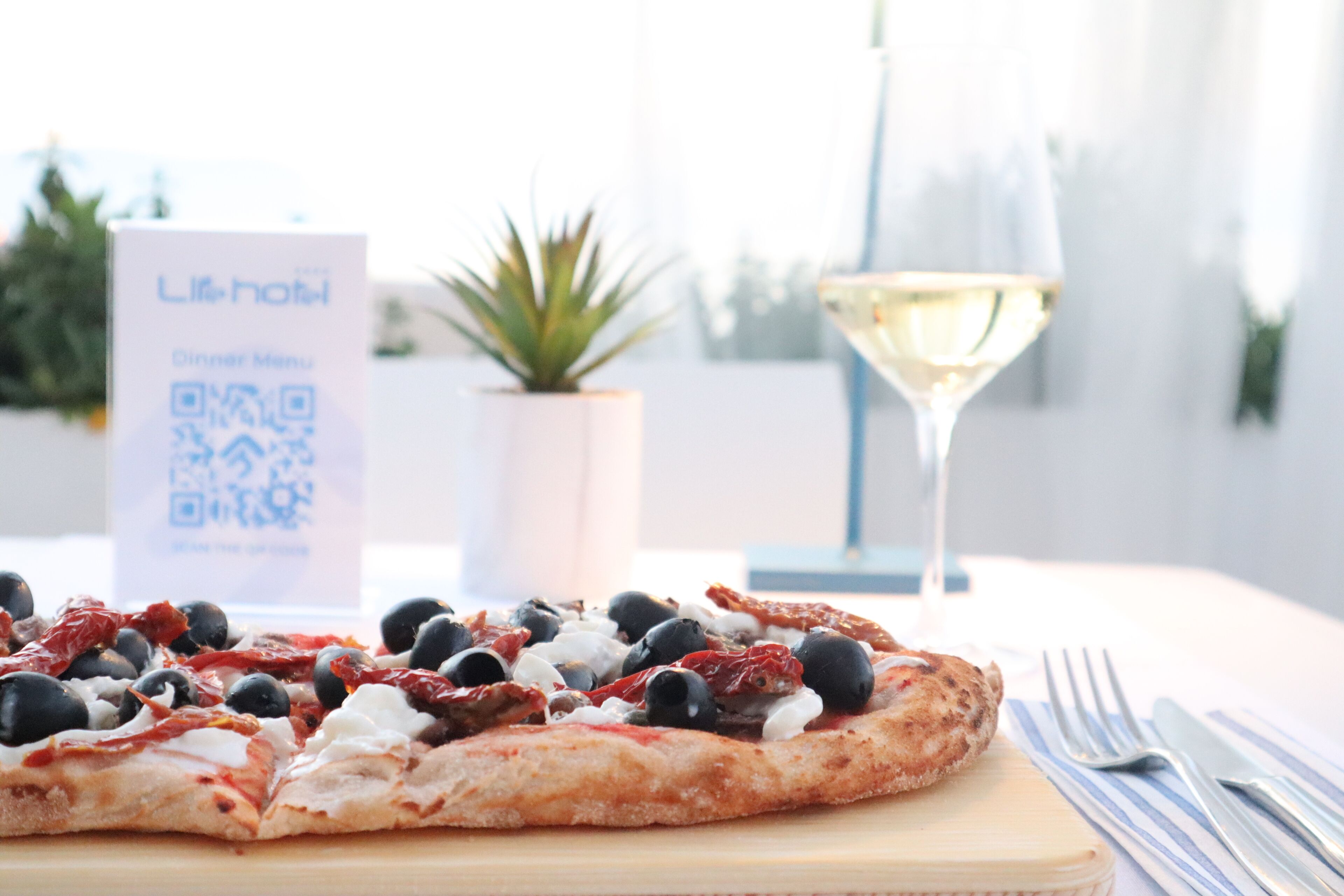 A pizza on a wooden board with a QR code sign in the background.
