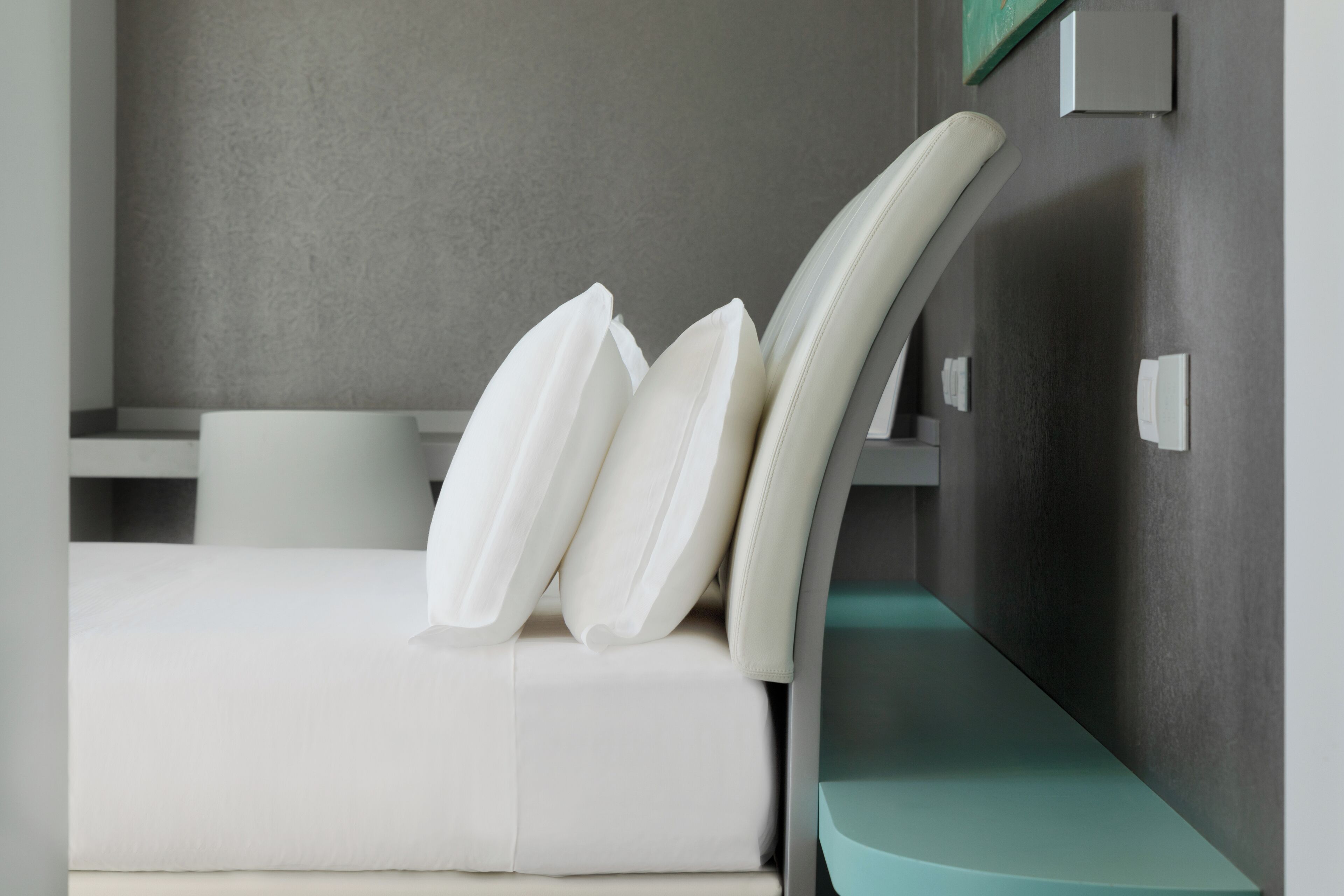 Una habitación de hotel moderna con una cama, almohadas blancas y una mesita de noche color turquesa.