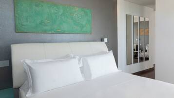 Una habitación de hotel moderna con una cama grande, ropa de cama blanca, un cuadro abstracto verde en la pared y un espejo que refleja la habitación.