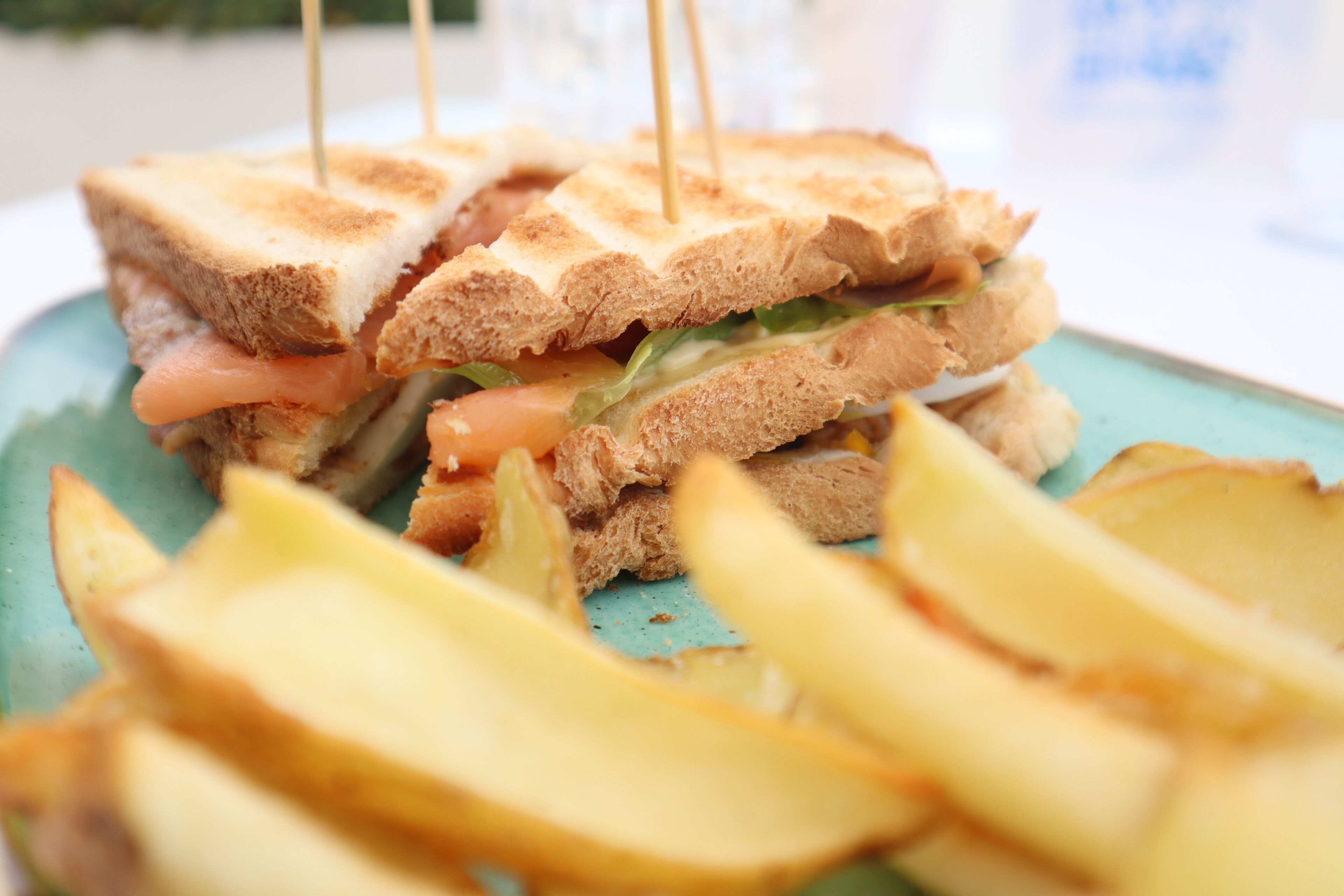 Un sándwich con palillos de dientes, lechuga y tomate, sobre un plato con papas a la francesa.