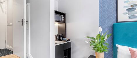 A modern room with a built-in microwave, a small kitchen area, and a seating area with a teal headboard and a potted plant.