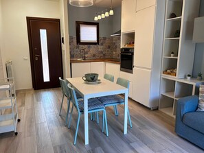 Een moderne keuken met witte kastjes, een ingebouwde oven en een eethoek met een tafel en stoelen.