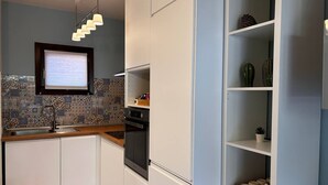 A modern kitchen with white cabinets, a built-in oven, and a wooden countertop. There is a window with blinds, a hanging light fixture, and a shelf with decorative items. - Tea House. Apartment surrounded by greenery with garden, near the center of Lucca (Lucca)