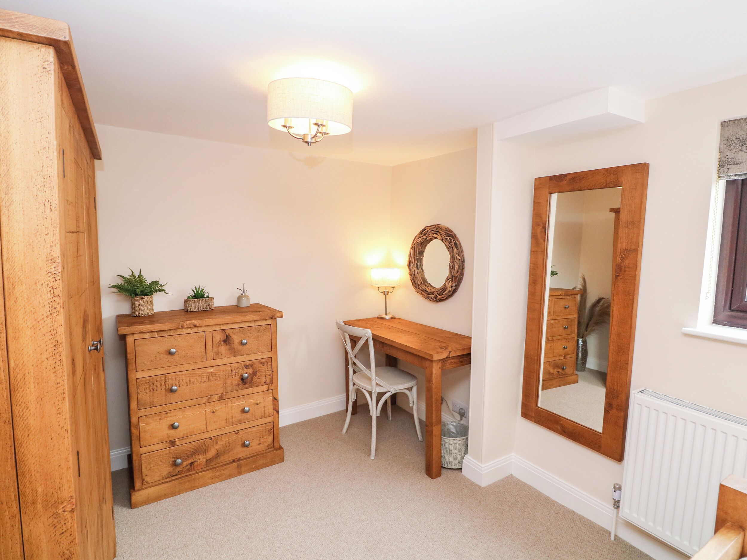 A room with a wooden dresser, a desk, a chair, a mirror, and a lamp.