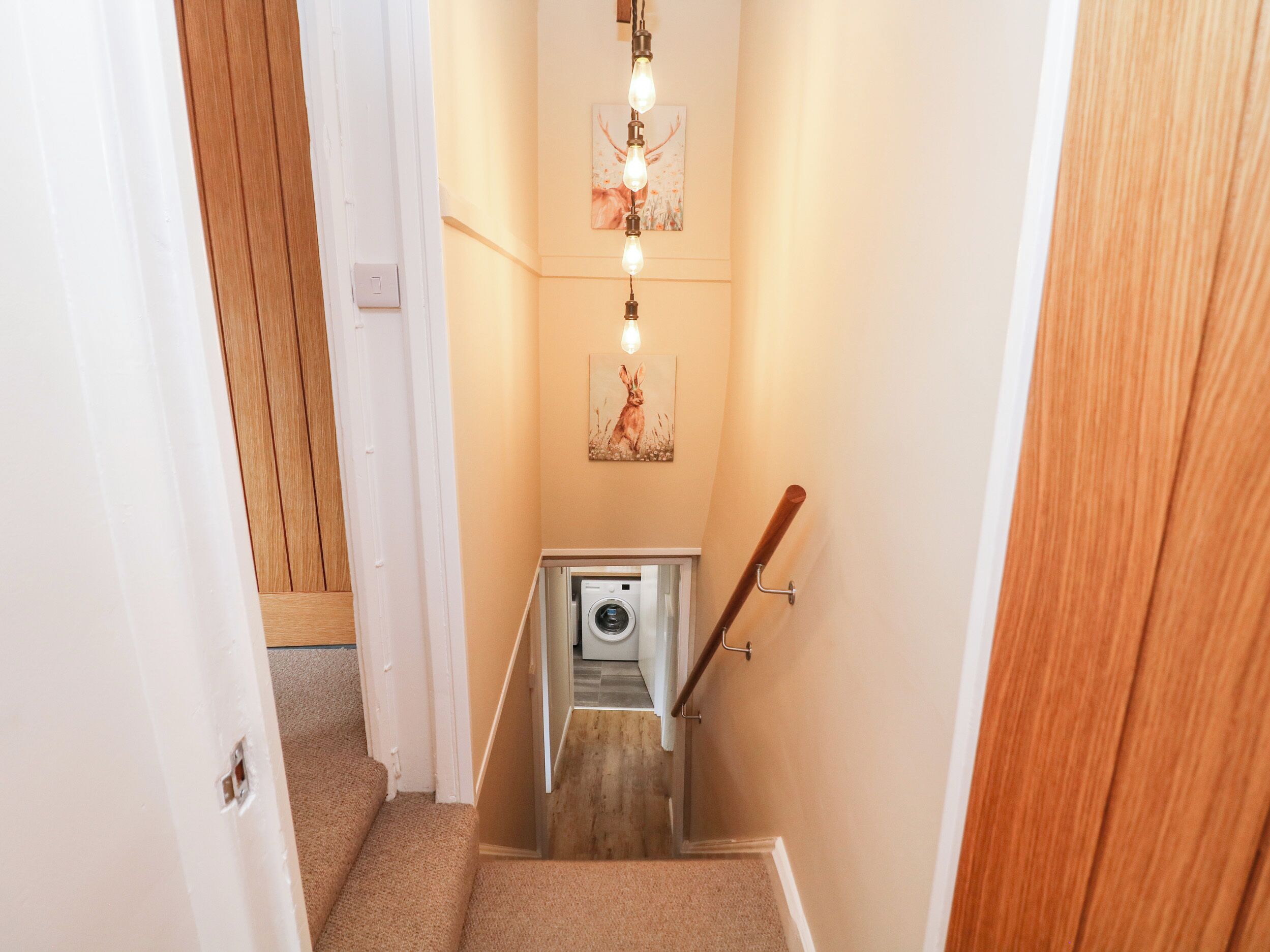 A narrow staircase with a washing machine at the bottom, wooden walls, and a light fixture with three bulbs.