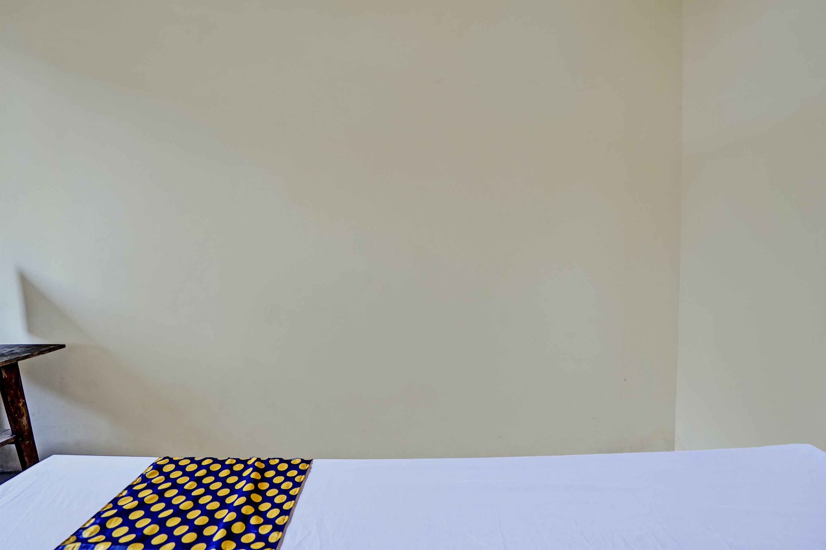 Een kamer met een bed, een witte muur en een klein tafeltje met een lamp.