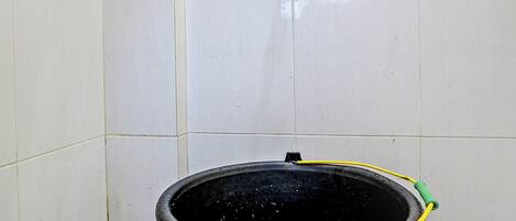A bathroom with white tiled walls, a black bucket with a yellow hose, and a floor with a drain.