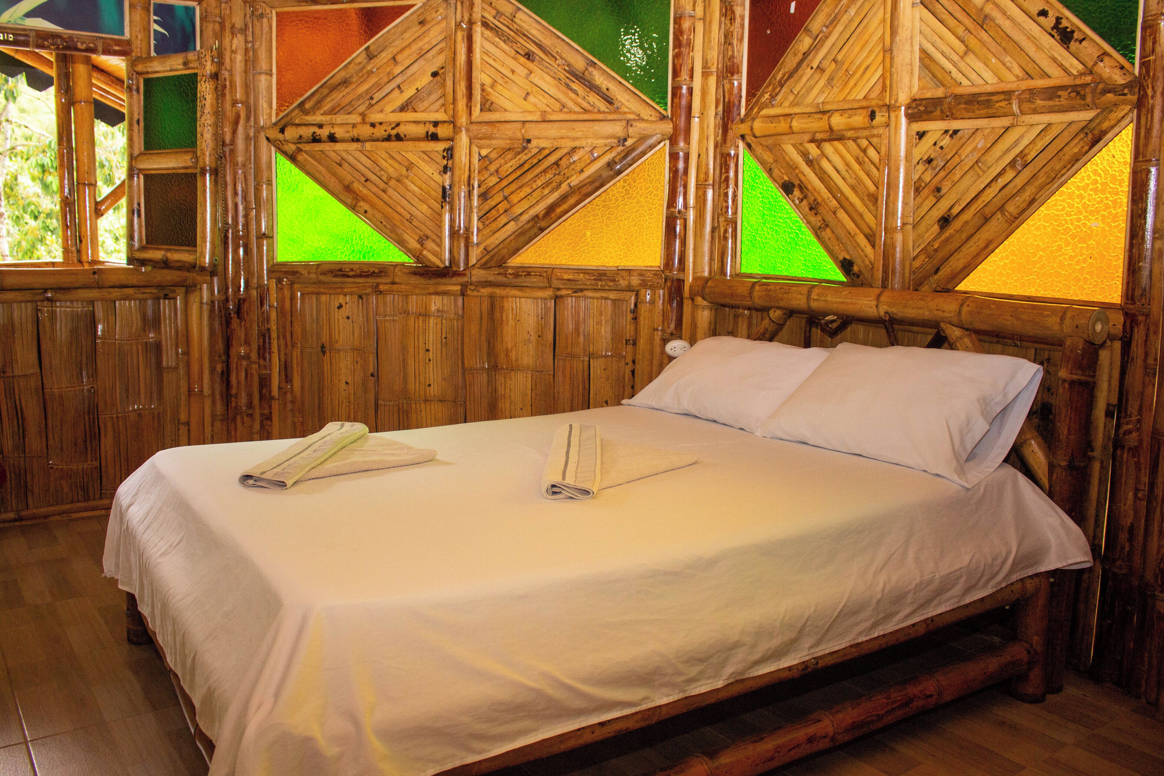 A wooden-framed bed with white linens, a wooden headboard, and a window with green-tinted glass panes.