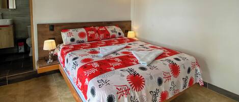 A neatly made bed with a red and white patterned bedspread, a wooden headboard, and two wall-mounted lamps.
