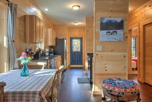 Interior de una cabaña de madera con comedor, cocina y una puerta que da a otra habitación.