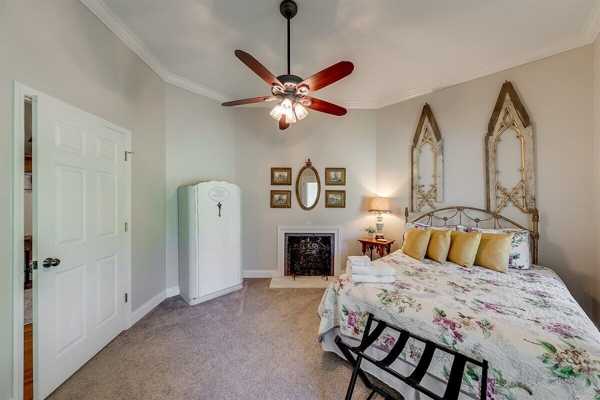 A bedroom with a bed, a ceiling fan, a fireplace, and a door.
