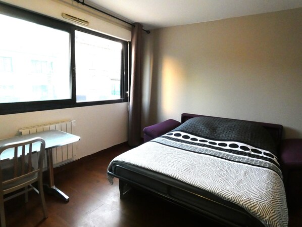 A bedroom with a bed, a desk, and a window.