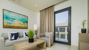 A modern living room with a sofa, a coffee table, a chair, a large abstract painting, a lamp, and a view through a large window.