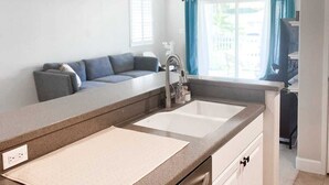 A modern kitchen with a central island, a built-in sink, and a window with curtains.
