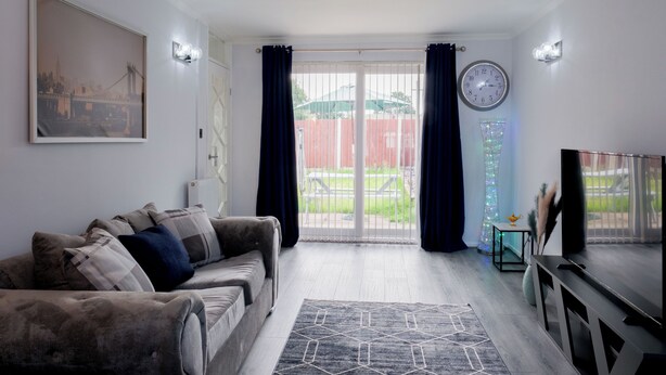 Een woonkamer met een bank, een televisie en een groot raam met gordijnen.