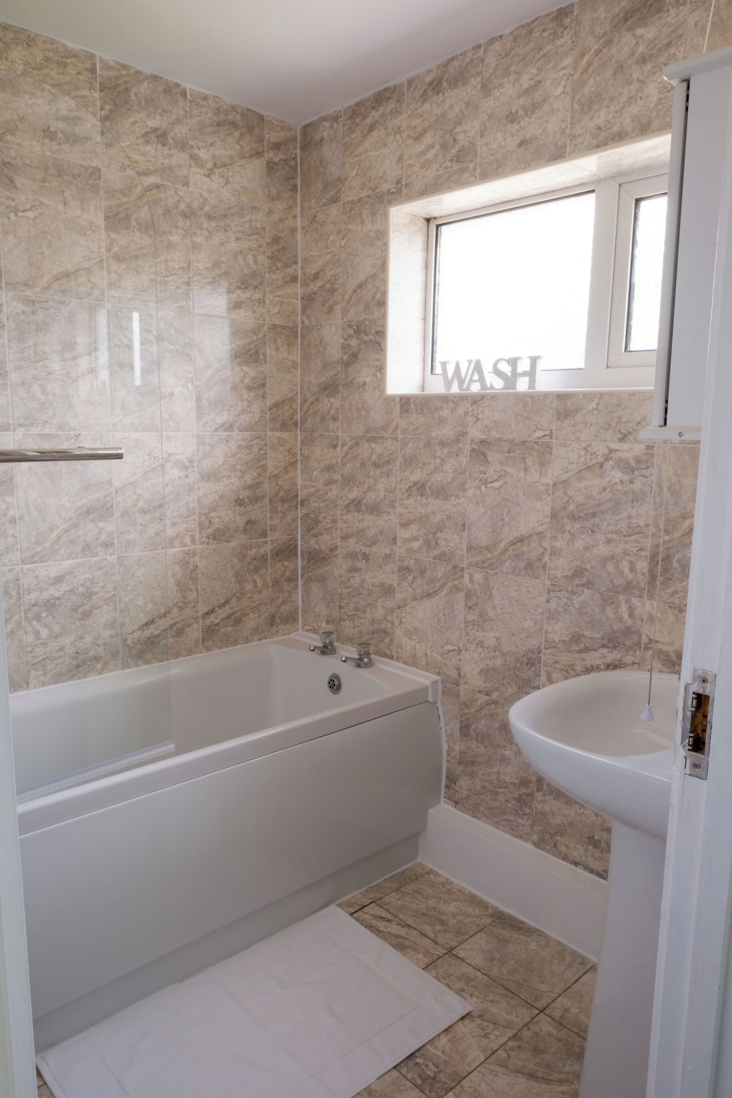 Casa de banho com banheira, pia e janela com o aviso 'WASH'.