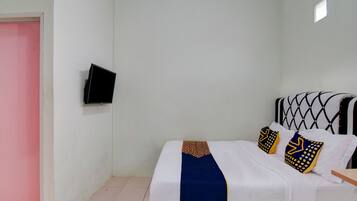 A single bed with a patterned bedspread and pillows, a television mounted on the wall, and a pink door.