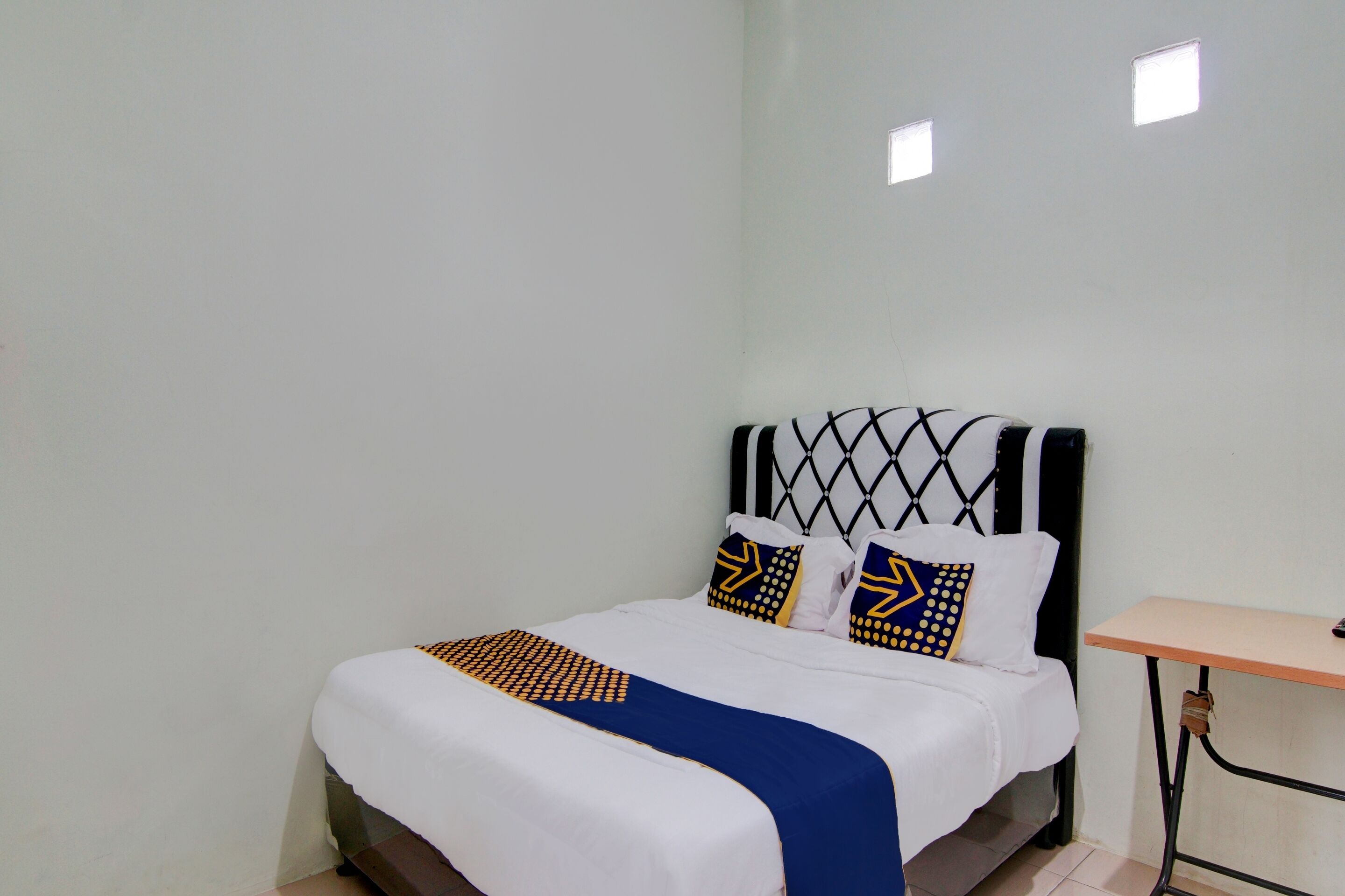 A neatly made bed with a patterned bedspread, two pillows with geometric designs, and a small table beside the bed.