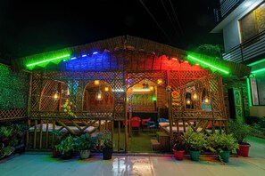 A covered outdoor seating area with bamboo lattice walls, potted plants, and hanging lights. - Orchid Hotel and Hostel (Narendranagar)