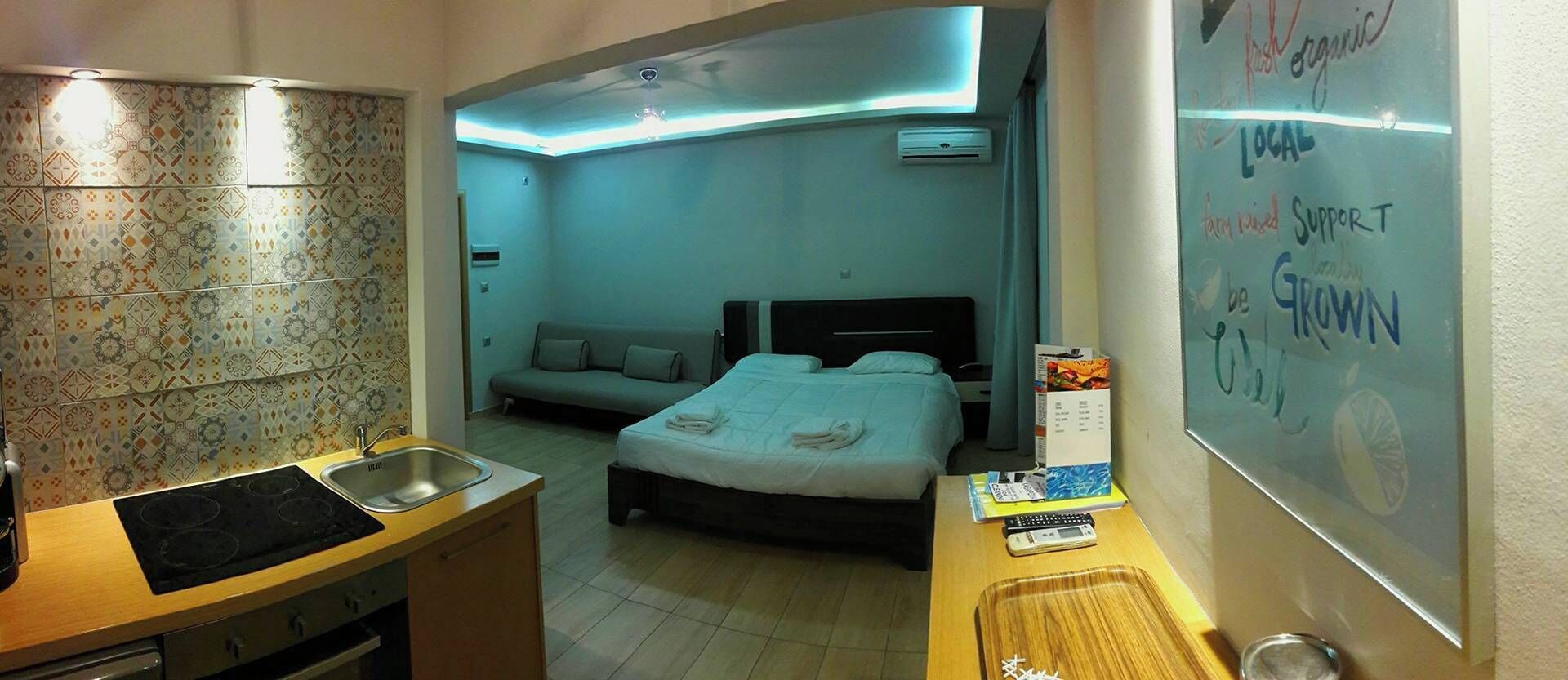 Habitación de hotel compacta con kitchenette, una cama, un sofá y una pared con mensajes motivacionales.