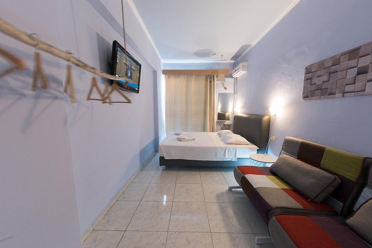 Habitació d'hotel amb un llit, un sofà, una televisió penjada a la paret i una finestra amb cortines.