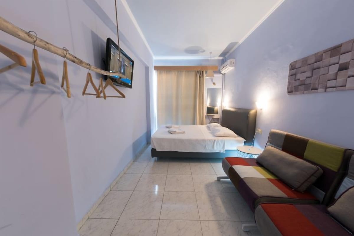 Una habitació d'hotel amb un llit, un sofà, una televisió i un televisor penjat a la paret.